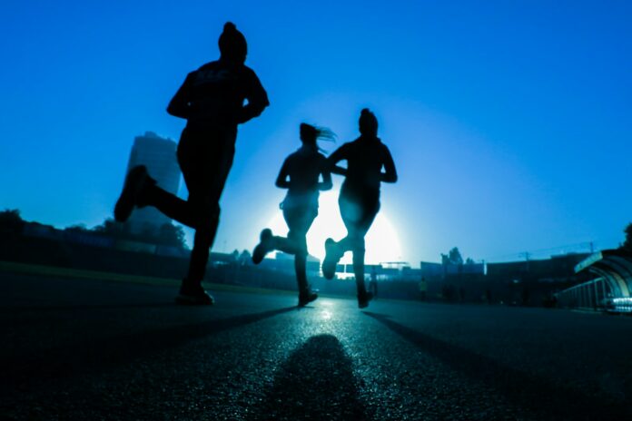 Photo by Fitsum Admasu silhouette of three women running on grey concrete road