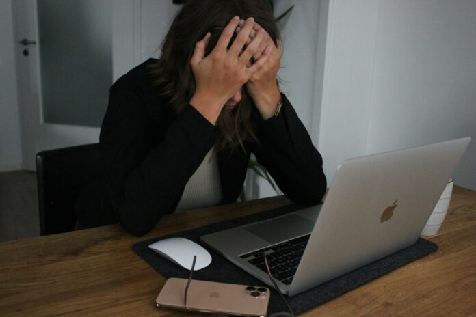 a woman covering her face while looking at a laptop